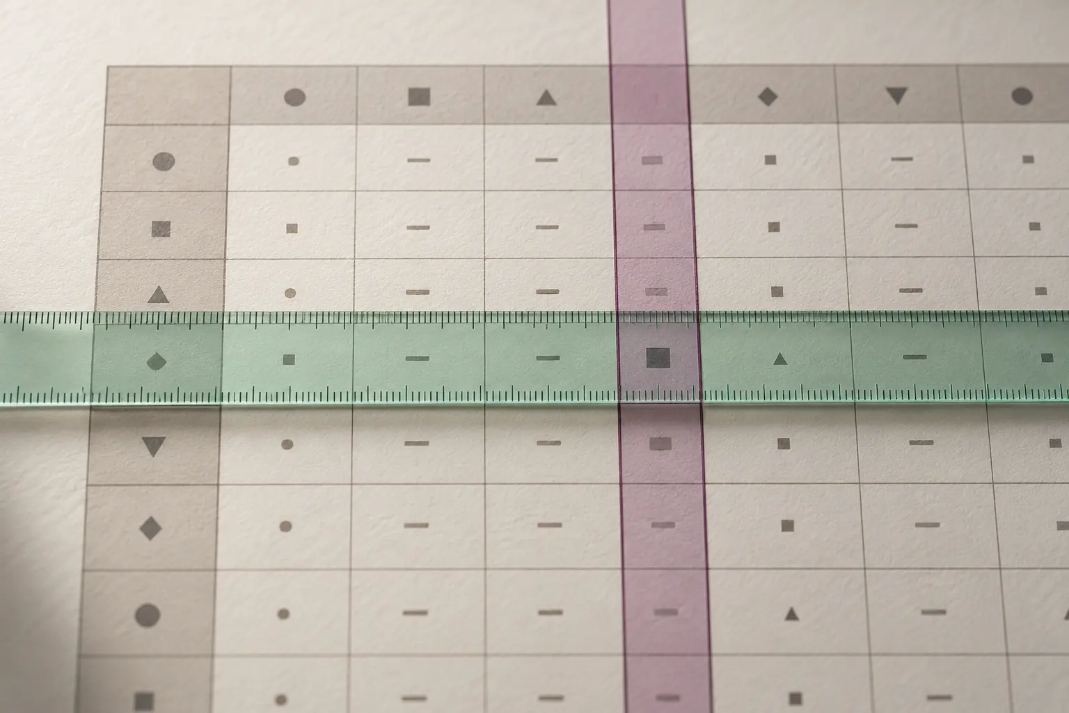 Deux guides transparents se croisent sur une cellule d’un tableau imprimé pour repérer sa ligne et sa colonne